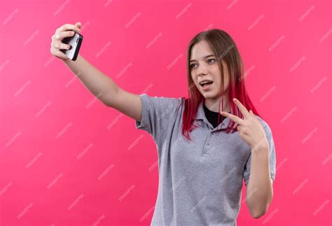 Free Photo Pleased Young Beautiful Girl Wearing Gray T Shirt Showing Peace Gesture And Taking