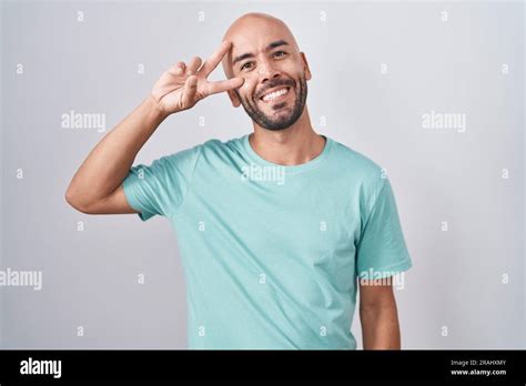 Middle Age Bald Man Standing Over White Background Doing Peace Symbol With Fingers Over Face