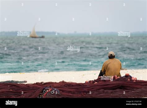 African Fisherman Sitting On Fishing Nets Looks Out To Sea Overcast