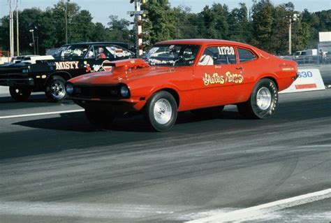 An Orange Car Driving Down The Road With Other Cars Behind It