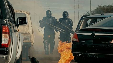 Two Men In Gas Masks Are Walking Away From A Car With Flames Coming Out