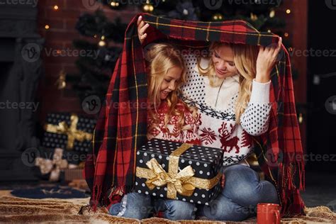 Mother And Daughter Sits Under Plaid With Ts Celebrating Christmas