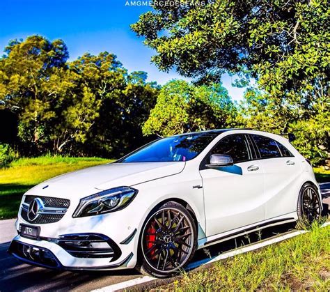 A White Mercedes Cla Parked On The Side Of The Road In Front Of Some Trees