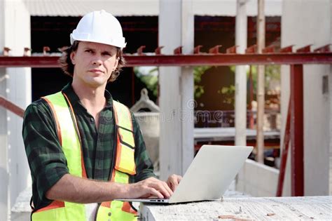 Portrait Of Happy Worker Engineer With Safety Vest And Helmet Typing On