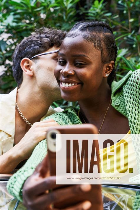 Stylish Young Man Kissing Black Girlfriend While Sitting At Table And