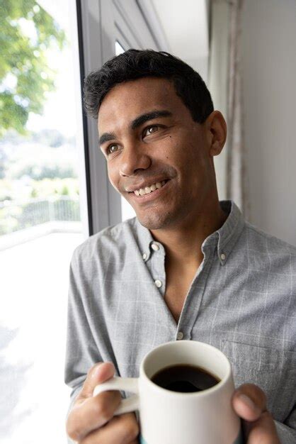 Premium Photo Happy Biracial Man Holding Mug Looking Through Window