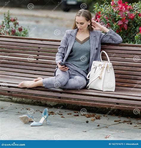 Barefoot Woman Sits On Bench In Park And Communicates On A Smartphone