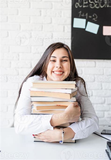 Young Teacher Sitting With Pile Of Books Looking Away Ready For Lesson