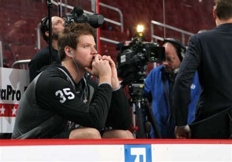 A Hockey Player Sitting On The Bench With His Hand To His Mouth And People Behind Him