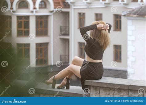 Slender Girl With Blonde Long Hair In Black Crop Top And Short Skirt Sits Outside And Adjusting