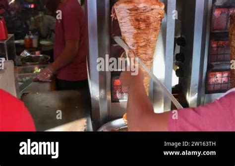 A Man Slicing Seasoned Chicken Meat From A Vertical Rotating Spit