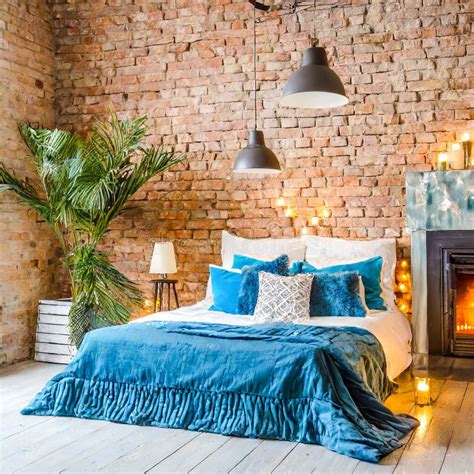 Bed With Blue Pillows And Coverlet Near Fireplace Against White Brick