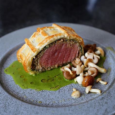 a piece of meat and vegetables on a plate with some nuts next to it,