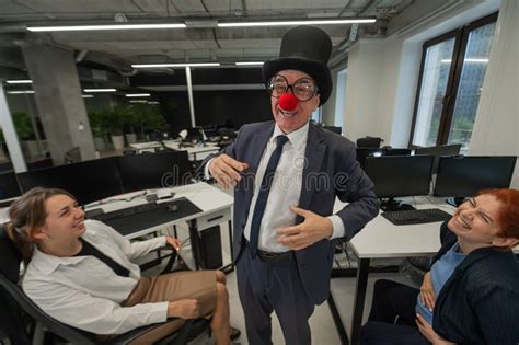 An Elderly Caucasian Man In A Clown Costume Amuses Two Caucasian Women