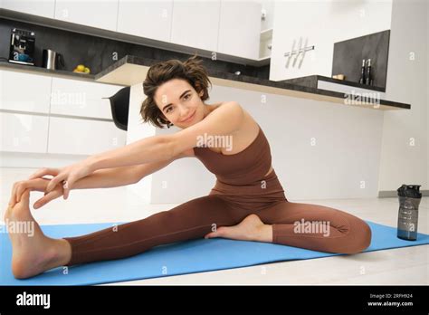 Portrait Of Fit Brunette Woman Fitness Instructor Doing Exercises At Home Stretches Her Legs