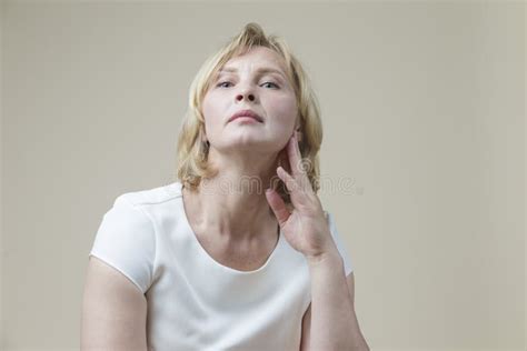 Mature Caucasian Blond Woman Posing In Casual Clothing With Lifted Hand Against Beige Background