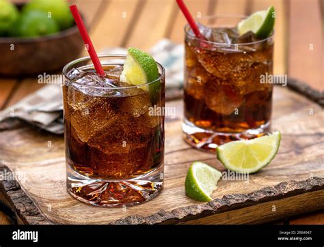 Rum And Cola Cocktail With Ice And Lime Slices On Rustic Wooden Tray