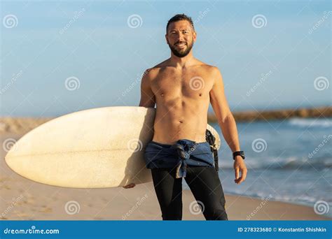 A Man Surfer With Naked Torso Standing On The Shore Holding A Surfing