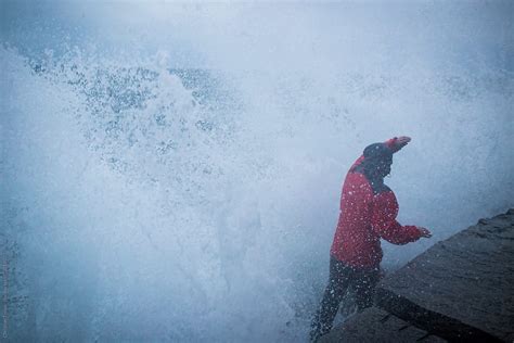 Man In Red Raincoat Getting Hit By Huge Wave On Breakwater By Stocksy