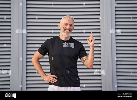 Cheerful Mature Man Smiling At Camera Raising Hand And Pointing Index