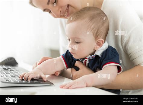 Cute Baby Boy Sitting On Mothers Lap In Office And Typing On Computer