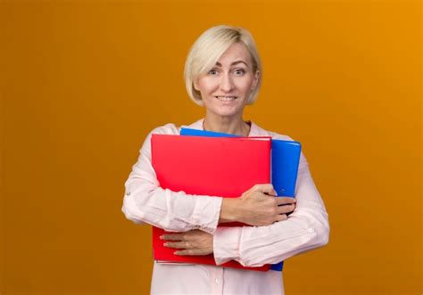 Souriante Jeune Femme Slave Blonde Tenant Des Dossiers Isolés Sur Un Mur Orange Photo Gratuite