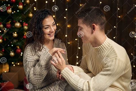 The Man Gives The Girl An Engagement Ring Couple Is In Christmas Lights And Decoration Dressed