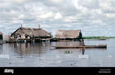 Boy In A Canoe Passes By Houses On The Flooded Sepik River Papua New