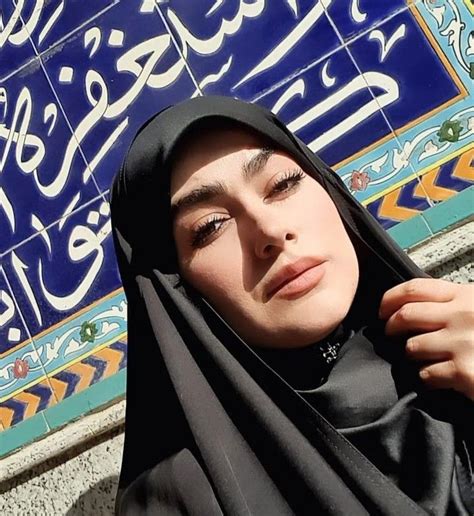 A Woman Wearing A Black Hijab Standing In Front Of A Blue Tile Wall