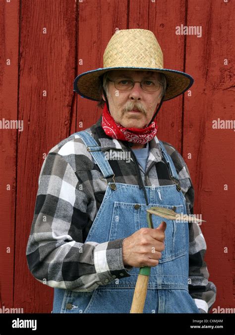 Farmer Holding A Garden Hoe Wearing Bib Overalls With A Barnboard