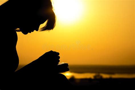 Silhouette Of The Hands Of Woman Praying To God In The Nature Witth The Bible At Sunset The