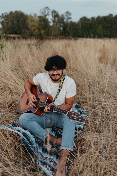 A Man Sitting In The Grass Playing An Acoustic Guitar