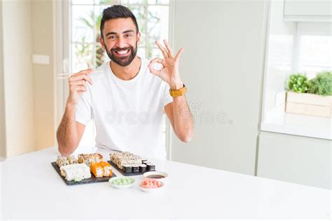 Handsome Hispanic Man Eating Asian Sushi Using Chopsticks Doing Ok Sign With Fingers Excellent