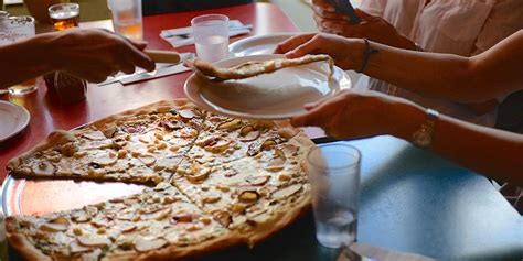 Three people sitting around a table sharing a large pizza pie in a ...