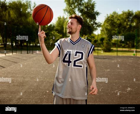 Man Spinning Basketball Ball On Finger Over Street Court Background