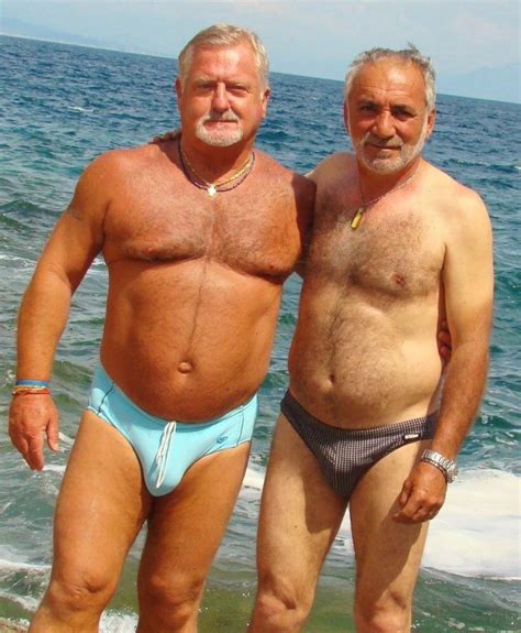 Two Older Men Standing Next To Each Other On Top Of A Beach Near The Ocean