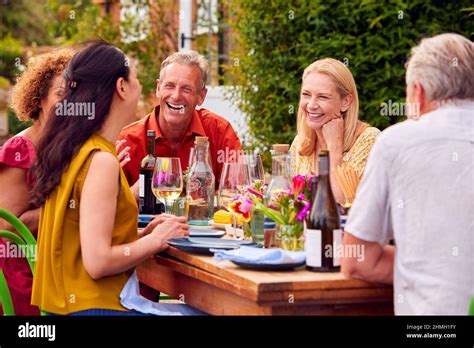 Group Of Mature Friends Talking Around Table At Summer Dinner Party In