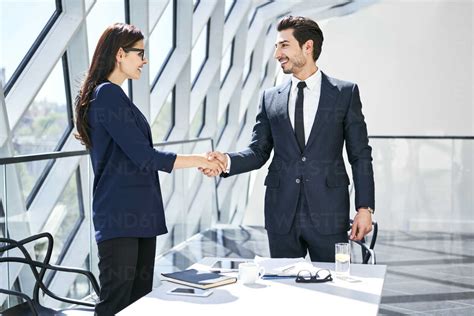 Businesswoman And Businessman Shaking Hands In Modern Office Stock Photo