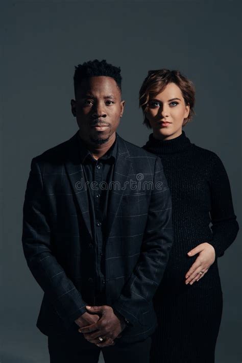 Young African Man And His Caucasian Pregnant Woman Stand Against Grey