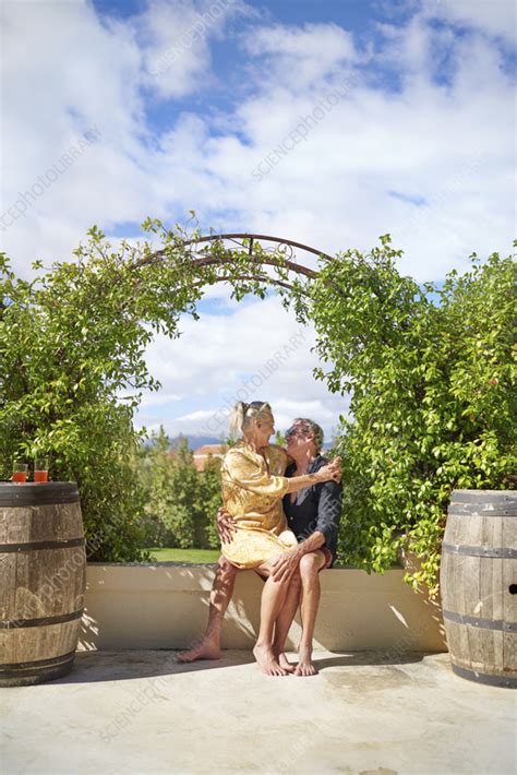 Senior Couple Hugging Under Trellis On Sunny Patio Stock Image F037