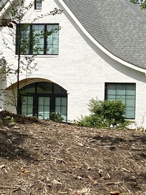 A White House Sitting On The Side Of A Hill Next To A Tree And Bushes