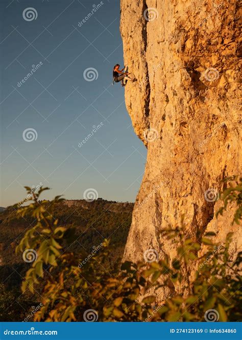 Vertical Female Rock Climber Scales A Towering Cliff In The Sunlit