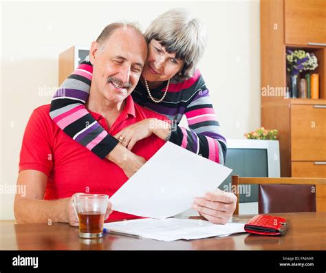 Cheeful Mature Man With Wife Reading Financial Documents At Table Stock