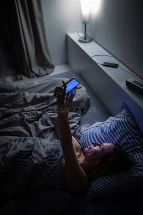 Pretty Middle Aged Woman Using Her Cell Phone In Bed At Night Stock