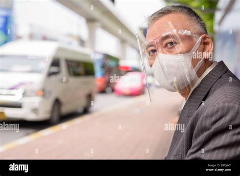 Mature Japanese Businessman With Mask And Face Shield Sitting At The