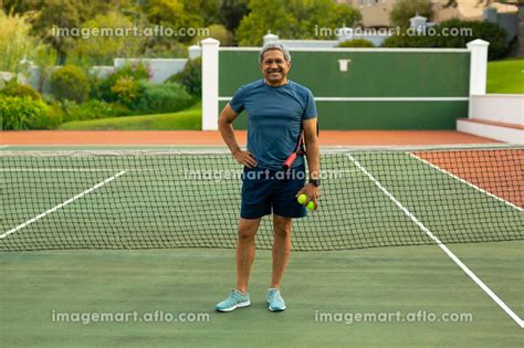 Portrait Of Smiling Biracial Senior Man Holding Balls And Racket