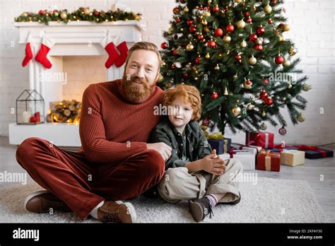 Redhead Father And Son Sitting With Crossed Legs On Floor In Living