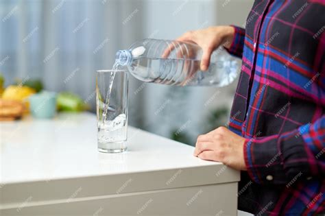 Женская рука держит бутылку с питьевой водой и наливает воду в стакан ...
