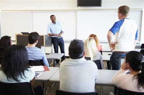 Male Tutor Teaching University Students In Classroom Background