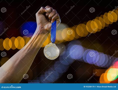 Mano Que Lleva A Cabo Triunfo De La Medalla Con El Fondo Ligero Chispeante Del Bokeh Foto De